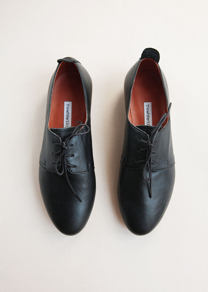 classic black leather daerby shoes from top on cream background