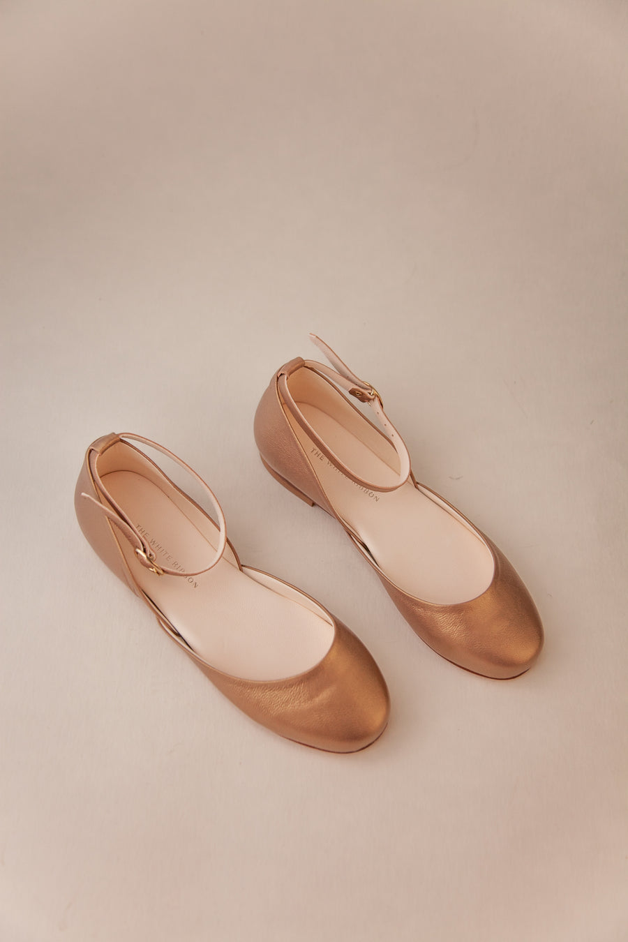 Pair of bronze shoes with white soles on a beige background