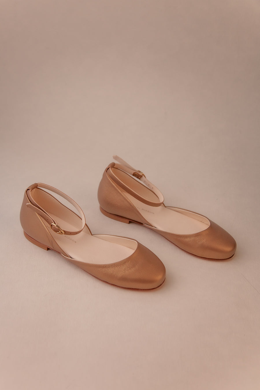 Pair of bronze gold shoes on a beige background