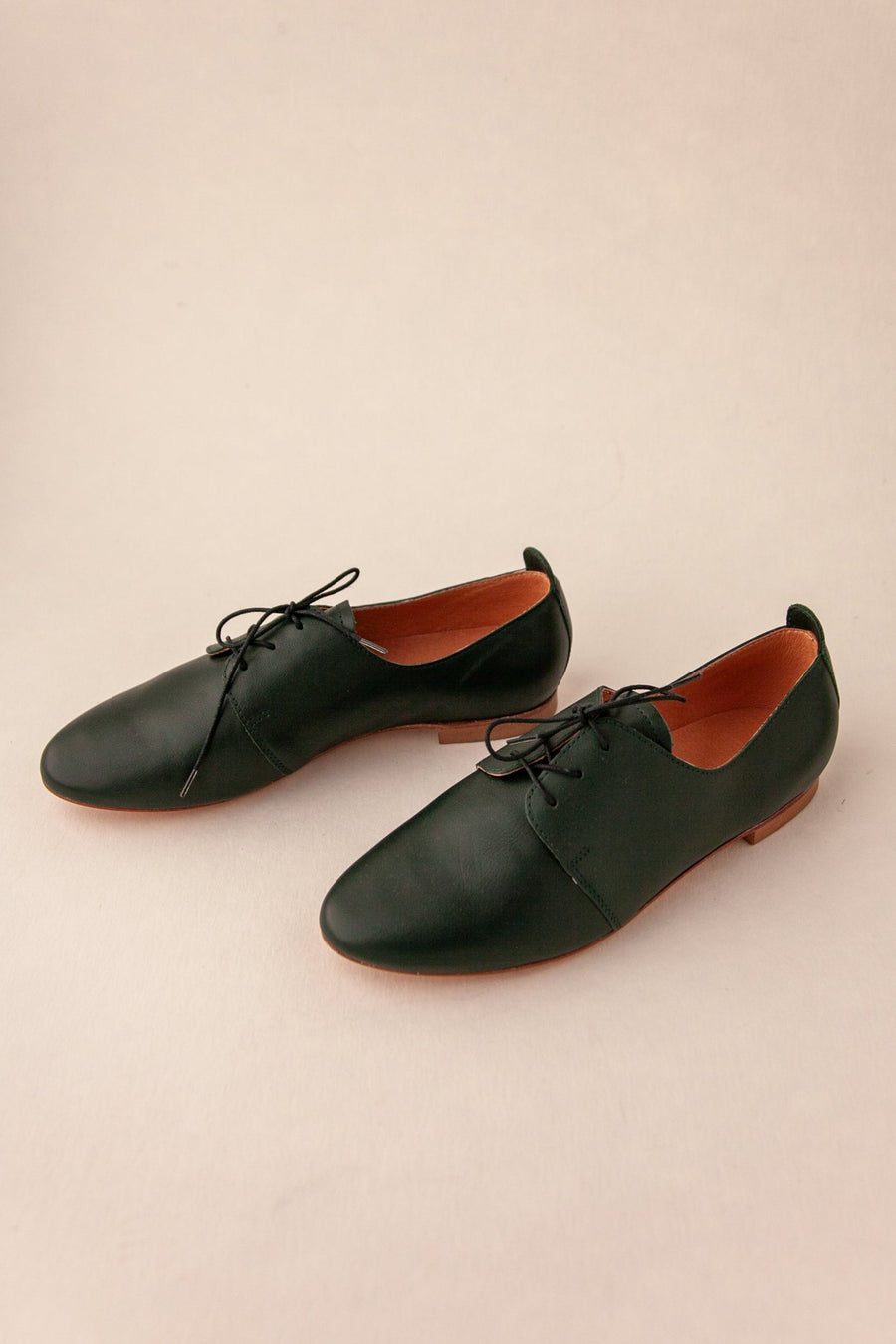 Pair of dark green leather shoes with brown soles on a beige background