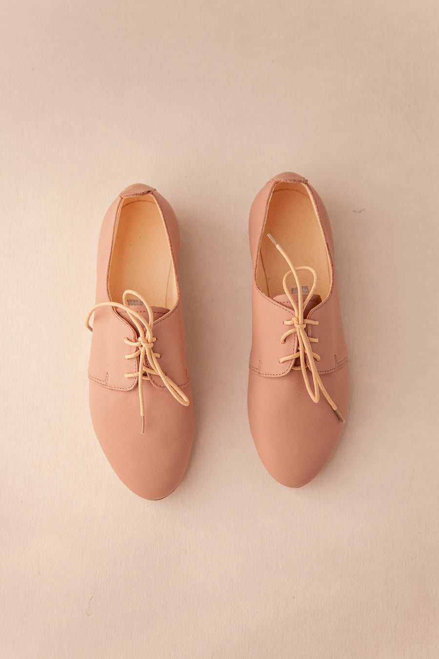 Pair of nude blush shoes with yellow laces on a beige background