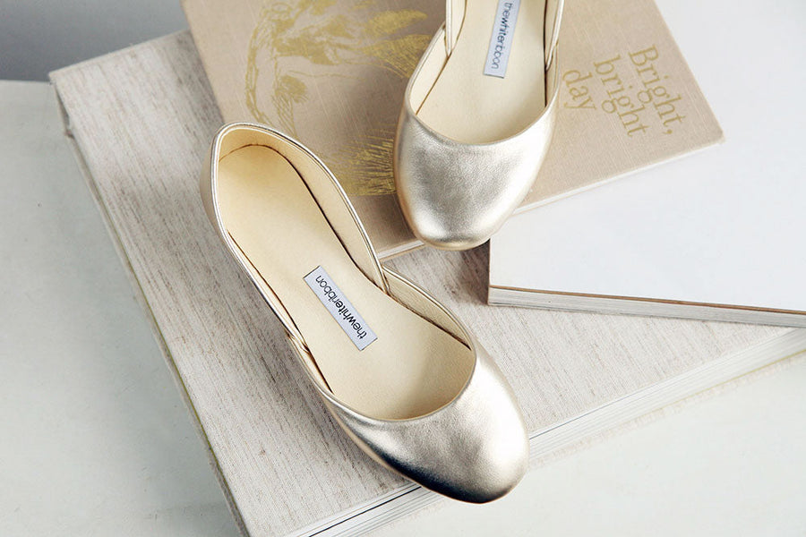 Close up of a pair of gold ballet flats on top of three books. 