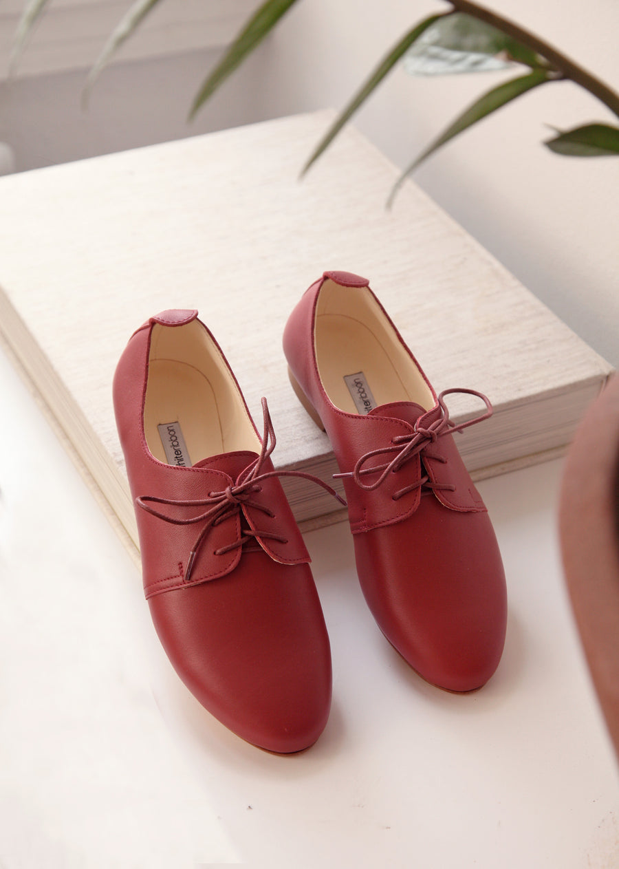 Dark red derby leather shoes placed on a book in a white background. 