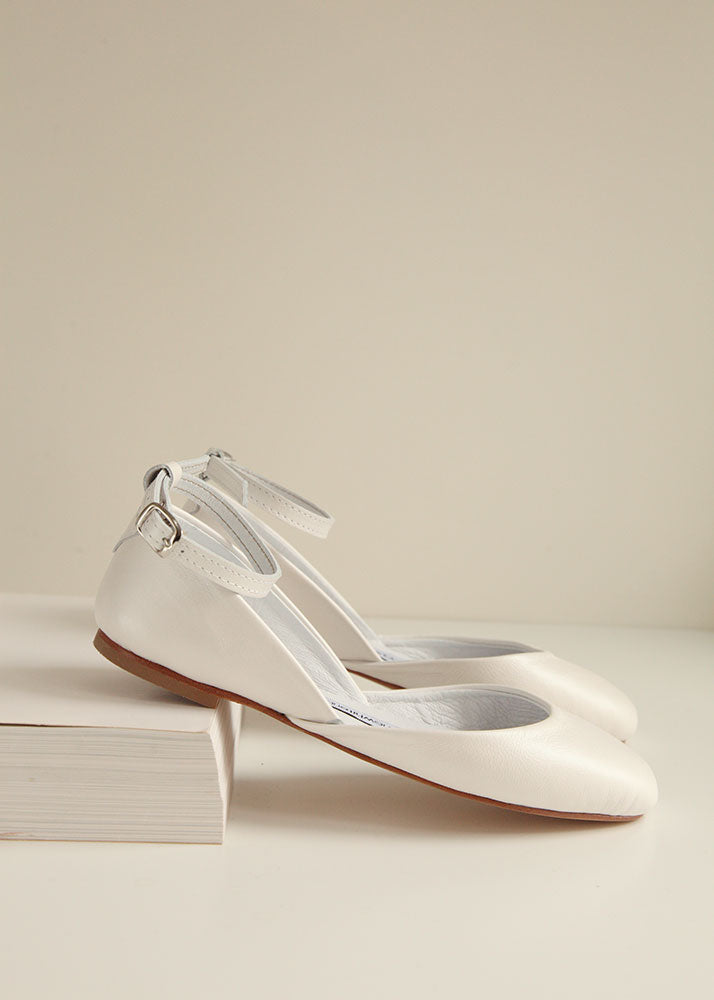 Bridal ballet flats in pearl ivory, shown from sideview, placed on a white book. 