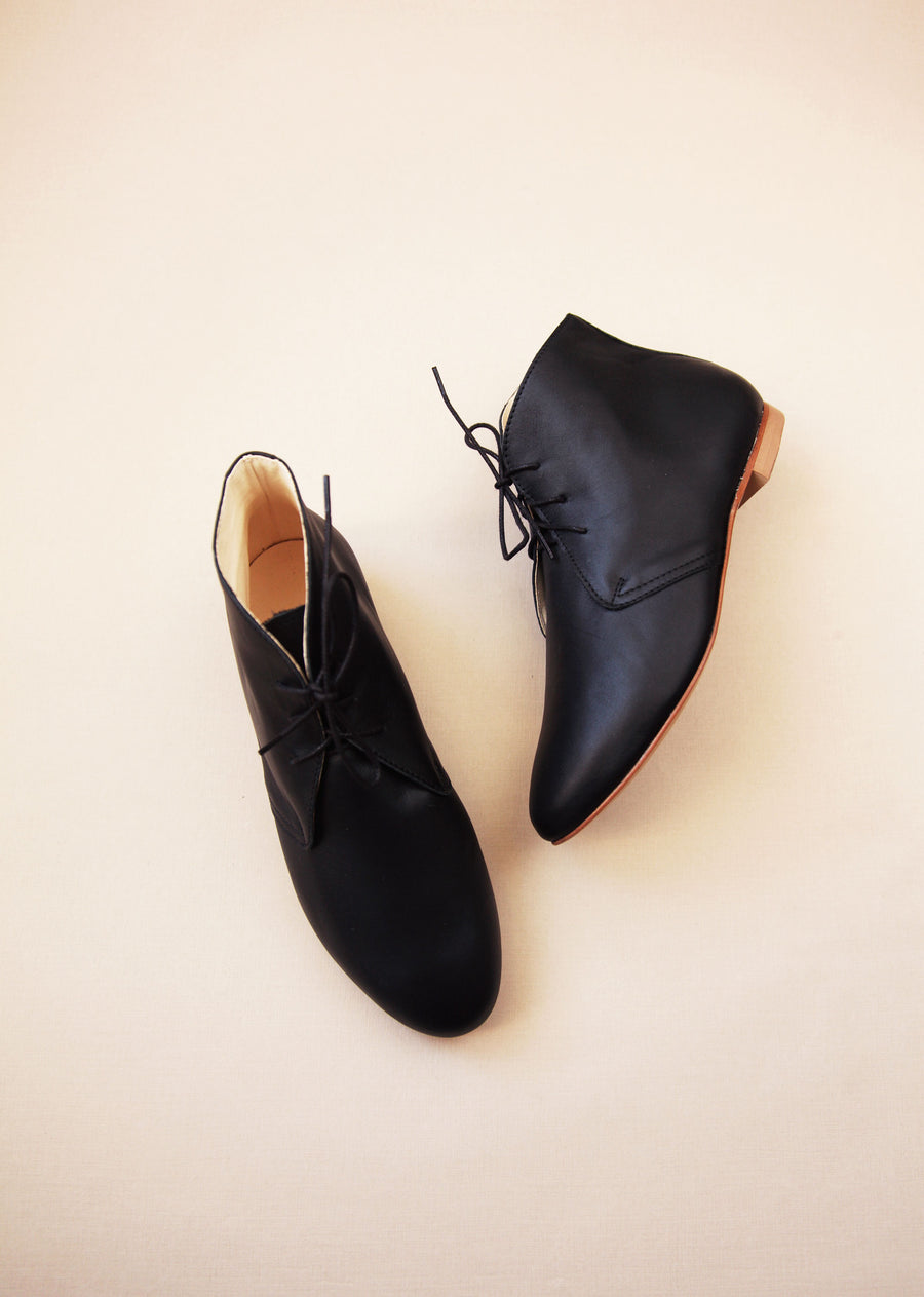 side and top view of smooth leather boots in black with cream background