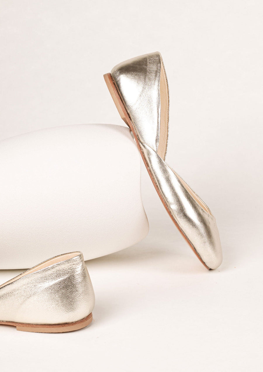 gold leather ballet flats against a white vase in sideview
