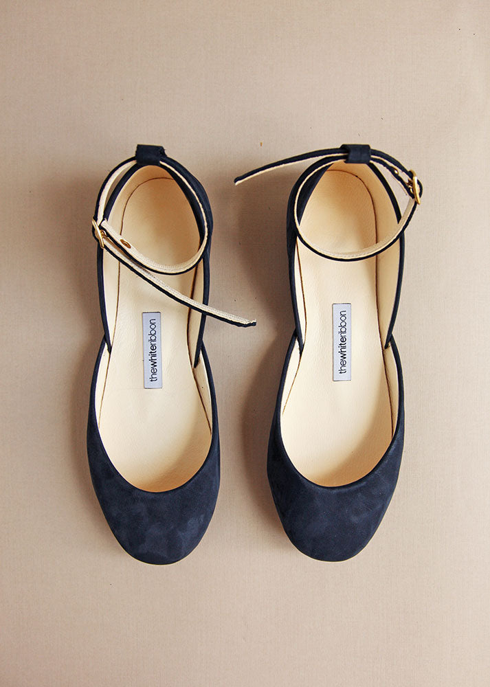 top shot of navy blue leather ballet flats with leather straps on cream background 